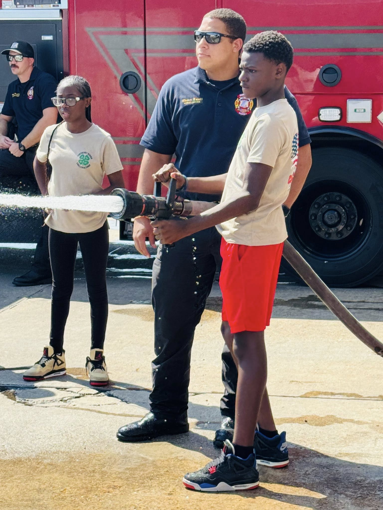 A fireman letting a boy work the firehose.